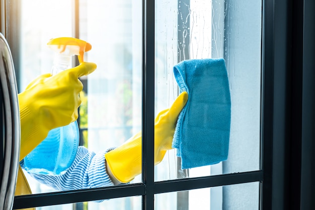 Concept de ménage et de nettoyage de femme, heureuse jeune femme essuyant la poussière à l'aide d'un pulvérisateur et d'un plumeau lors du nettoyage en verre à la maison