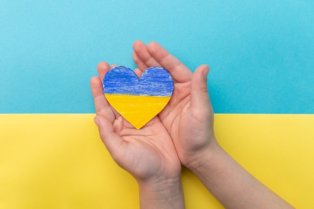 Le concept de mettre fin à la guerre en Ukraine Coeur aux couleurs du drapeau de l'Ukraine entre les mains d'un enfant