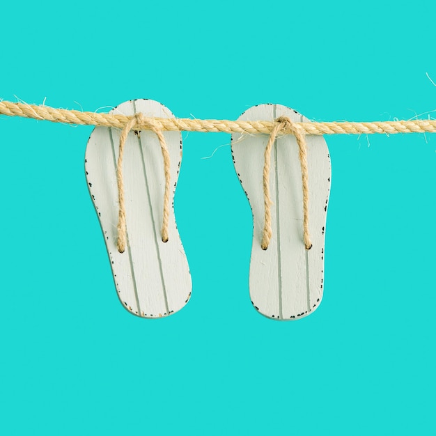 Concept minimal de vacances d'été avec des tongs de chaussures de plage suspendues à une corde avec un fond turquoise