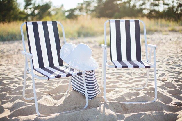 concept de mobilier et de vacances d'été - deux salons de plage avec sac de plage et chapeau blanc sur la plage