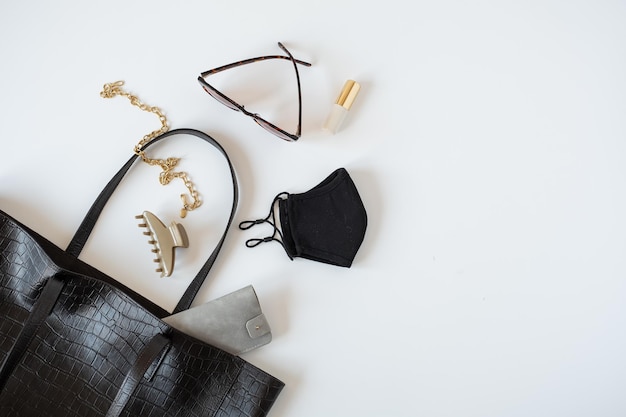 Concept de mode avec accessoires pour femmes Sac en cuir noir masque lunettes de soleil collier barrette sur fond de tableau blanc Vue de dessus à plat vue de dessus minimal blog de mode féminine modèle de médias sociaux