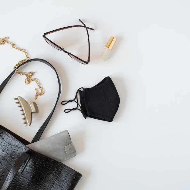 Concept de mode avec accessoires pour femmes Sac en cuir noir masque lunettes de soleil collier barrette sur fond de tableau blanc Vue de dessus à plat vue de dessus minimal blog de mode féminine modèle de médias sociaux