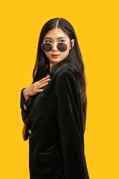 Concept de mode femme à la mode porter un manteau noir et des lunettes de soleil pour poser sur fond jaune