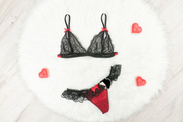 Concept de mode Soutien-gorge et culotte en dentelle noire sur fourrure blanche. Bougies rouges en forme de coeur