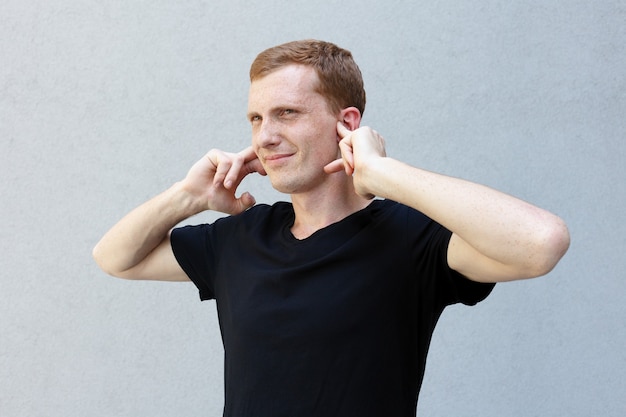 Concept de mode, de style, d'émotions et de personnes - Portrait en gros plan d'une rousse d'un beau mec viril avec des taches de rousseur. fronçant les sourcils, fermant les oreilles avec les paumes, agacé et fatigué du bruit