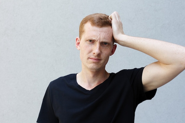 Concept de mode, de style, d'émotions et de personnes - Portrait en gros plan d'une rousse d'un beau mec viril avec des taches de rousseur sur un T-shirt noir à fond gris. expression effrayée essayant de se souvenir