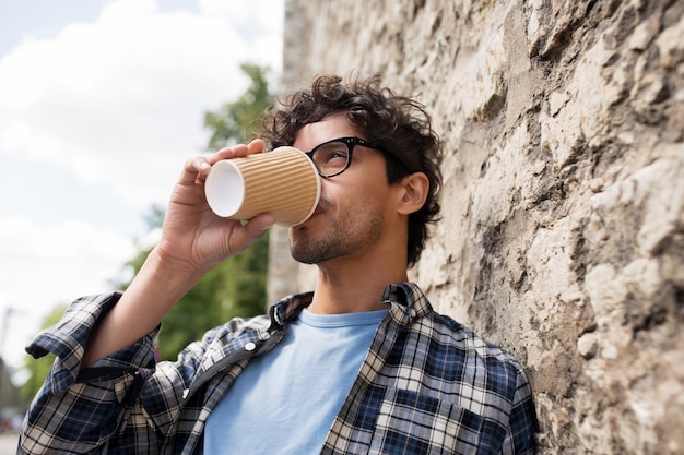 concept de mode de vie, de boissons et de personnes - homme à lunettes buvant du café à partir d'une tasse de papier jetable sur un mur de rue en pierre