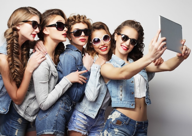 Concept de mode de vie et de personnes : cinq amis filles hipster prenant selfie avec tablette numérique, tourné en studio sur fond gris