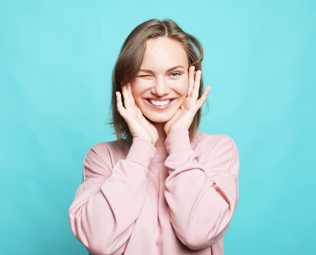 Concept de mode de vie et de personnes Jeune femme blonde souriante et heureuse aux cheveux courts portant un pull rose sur fond bleu