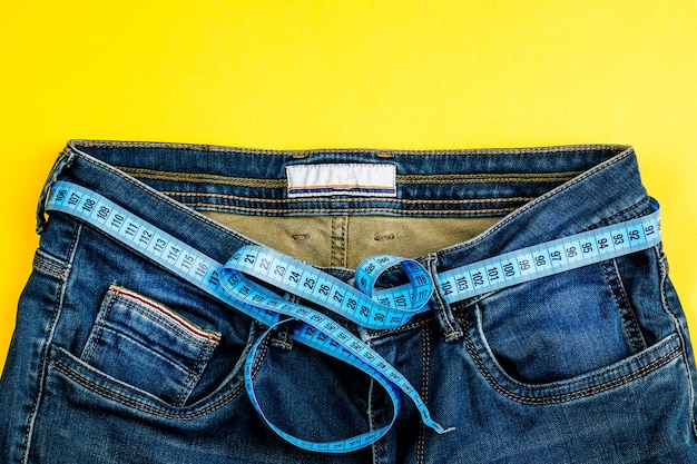 Le concept d'un mode de vie et d'un régime alimentaire sains. Jean bleu avec un ruban à mesurer bleu au lieu d'une ceinture.