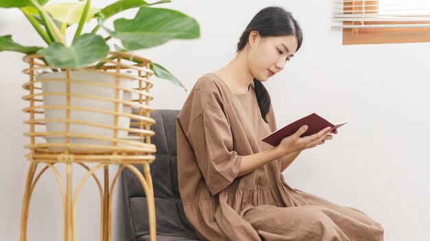 Concept de mode de vie de relaxation Jeune femme asiatique lisant un livre assis pour se détendre dans le salon