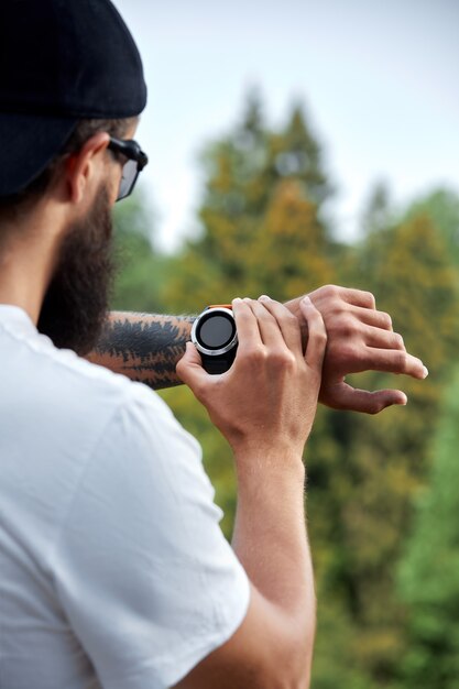 Concept de mode de vie sain et intelligent. Athlète musclé faisant de l'exercice à l'extérieur dans un parc ensoleillé. Jeune bel homme en vêtements de sport vérifiant la montre de suivi de sport.