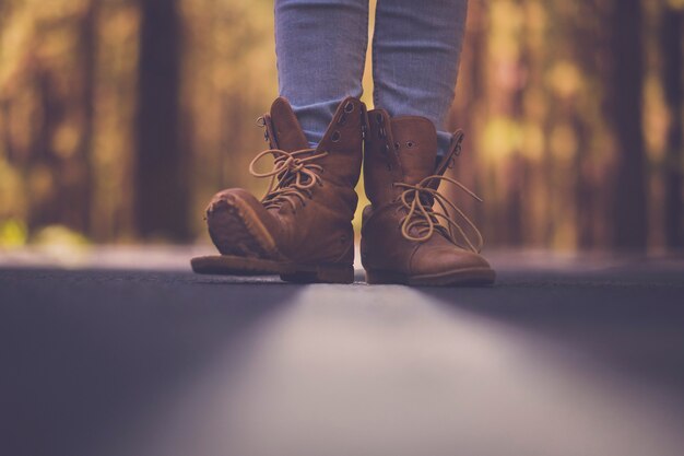 Concept de mode de vie de voyage - point de vue au sol avec route goudronnée défocalisée et gros plan sur une vieille paire de chaussures de marche de trekking cassées