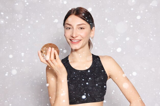 Concept de neige, hiver, noël, santé, personnes, nourriture et beauté - Belle jeune fille avec un maquillage naturel léger et une peau parfaite avec de la noix de coco à la main sur fond de neige