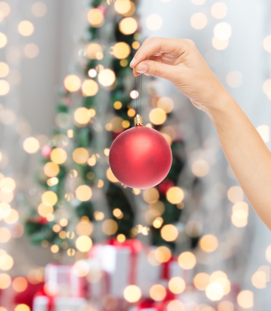 concept de noël, de décoration, de vacances et de personnes - gros plan d'une main de femme tenant une boule de noël sur fond de lumières d'arbre