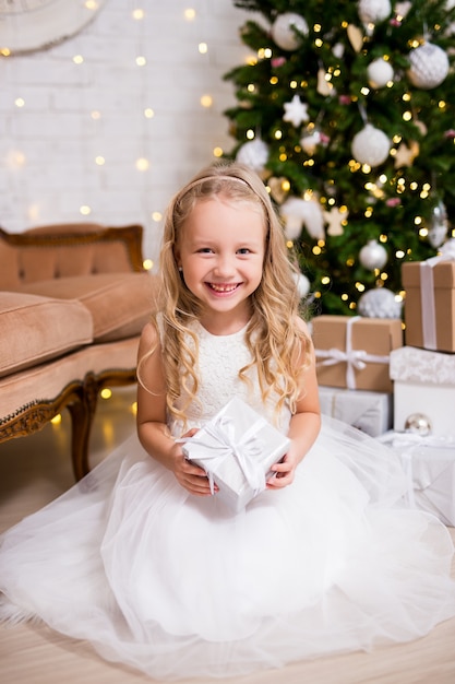 Concept de Noël et du nouvel an mignonne petite fille en robe blanche ouvrant des cadeaux de Noël