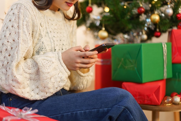 Concept de noël Une femme asiatique est assise dans un salon décoré de noël et discute sur un smartphone