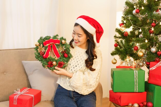 Concept de noël Une femme asiatique tient une couronne de décoration avec des branches de sapin et des décorations de noël