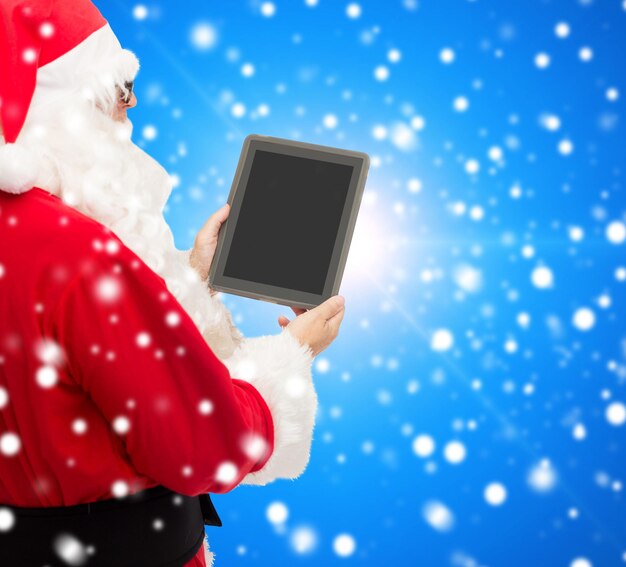 concept de noël, de publicité, de technologie et de personnes - homme en costume de père noël avec tablette pc sur fond bleu neigeux