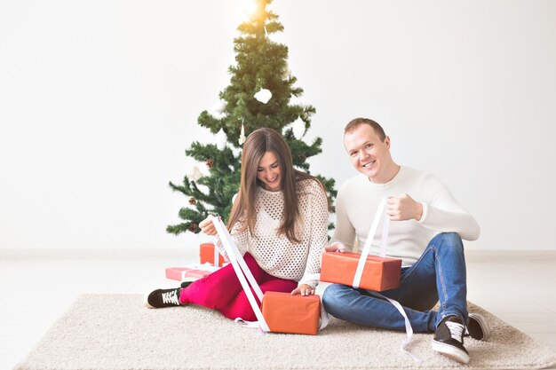 Concept de Noël, de vacances et de célébration - Beau jeune homme et jolie jeune femme assis sur le tapis et tenant un coffret cadeau.