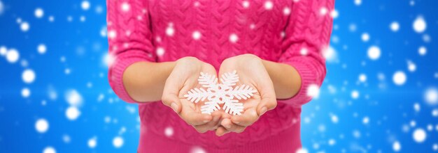 concept de noël, de vacances et de personnes - gros plan d'une femme en pull rose tenant un flocon de neige sur fond bleu neigeux