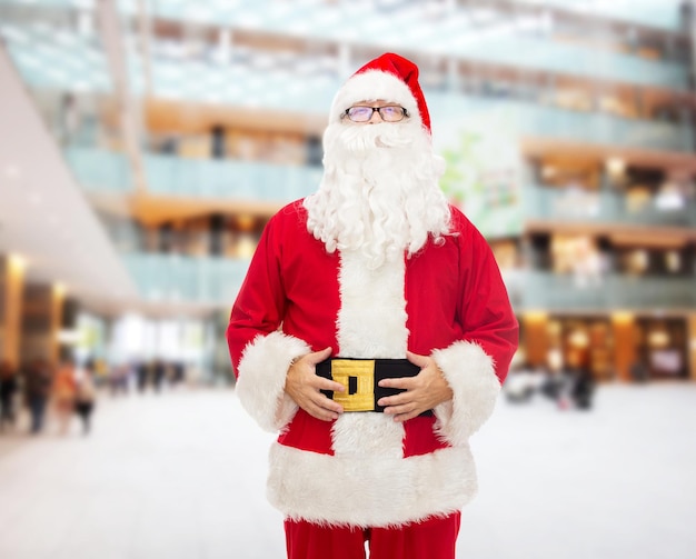 concept de noël, de vacances et de personnes - homme en costume de père noël sur fond de centre commercial