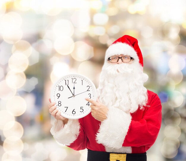 concept de noël, de vacances et de personnes - homme en costume de père noël avec horloge montrant douze doigts pointés sur fond de lumières