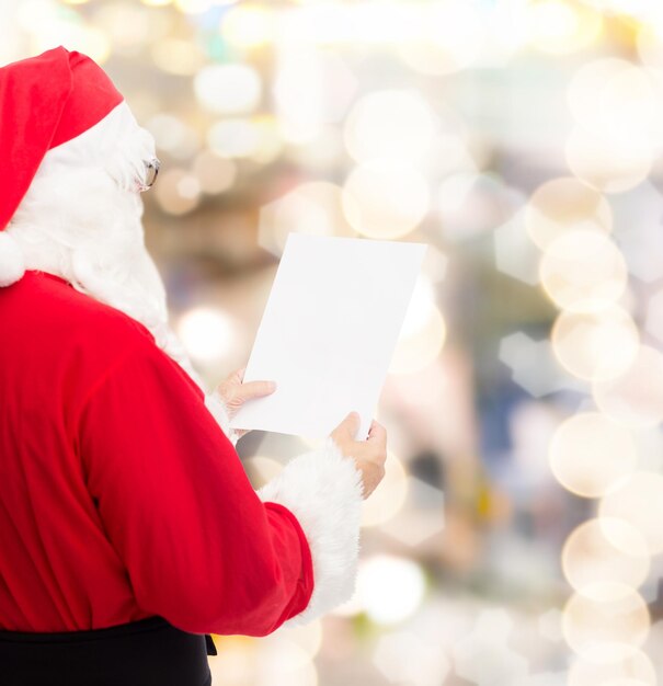 concept de noël, de vacances et de personnes - homme en costume de père noël lisant une lettre sur fond de lumières