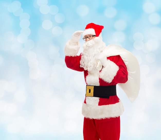 concept de noël, de vacances et de personnes - homme en costume de père noël avec sac regardant loin sur fond de lumières bleues