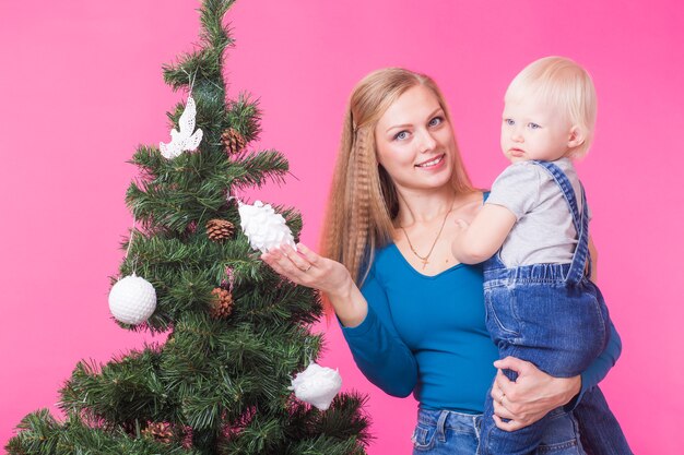 Concept de Noël, vacances et personnes - jeune femme heureuse avec sa fille sur les mains montrent des décorations sur l'arbre de Noël.