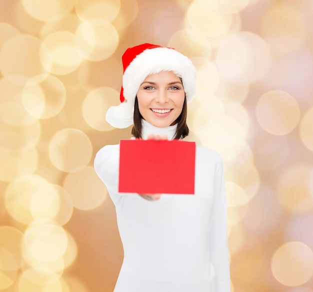 concept de noël, vacances, personnes, publicité et vente - femme heureuse en chapeau de santa helper avec carte rouge vierge sur fond de lumières beiges