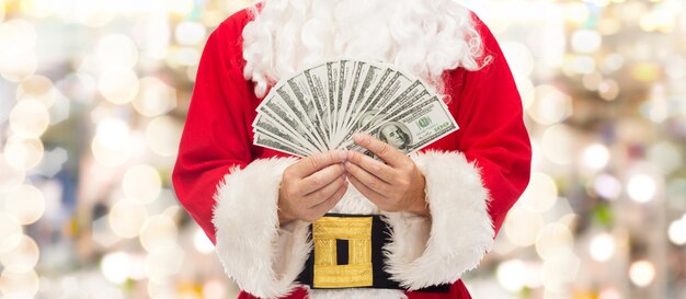 concept de noël, vacances, victoire, monnaie et personnes - gros plan du père noël avec de l'argent en dollars sur fond de lumières