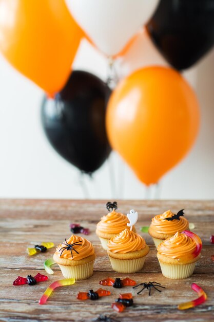 concept de nourriture, de boulangerie et de vacances - cupcakes ou muffins avec des décorations de fête d'Halloween et des bonbons à la gelée sur table en bois et des ballons