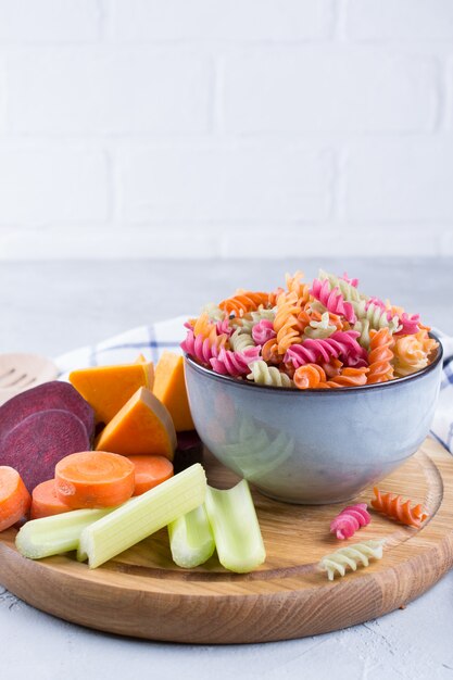 Concept de nourriture saine sans gluten. Pâtes sèches fusilli au riz à base de légumes dans un bol en céramique grise et ses colorants végétaux naturels céleri, betterave, carotte, citrouille, panais.