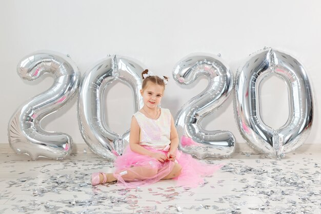 Concept de nouvel an, vacances et célébration - petite fille assise près de ballons numéros 2020