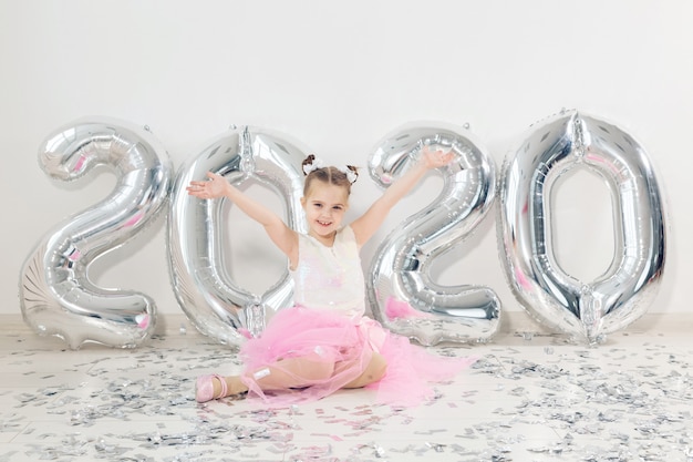 Concept de nouvel an, vacances et célébration - petite fille assise près de ballons numéros 2020