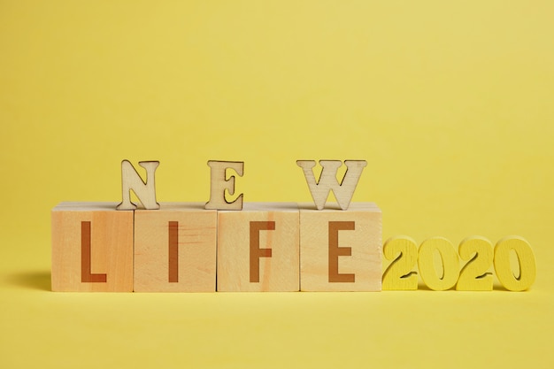 Photo le concept d'une nouvelle vie. chiffres en bois 2020 à côté de cubes avec des lettres sur fond jaune.