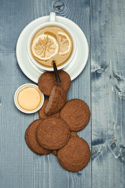 Concept de nutrition et de boisson chaude. Biscuits à l'avoine comme pâtisserie savoureuse pour une tasse de thé au citron et au miel. Biscuits près du thé sur fond de bois gris. Boulangerie sucrée et tea time.