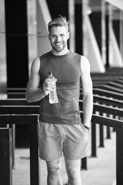 Concept de nutrition sportive. L'athlète d'homme tient le corps d'hydratation de soin de bouteille en plastique après l'entraînement. Boisson vitaminée rafraîchissante. L'athlète boit de l'eau après l'entraînement. L'apparence athlétique de l'homme tient une bouteille d'eau.
