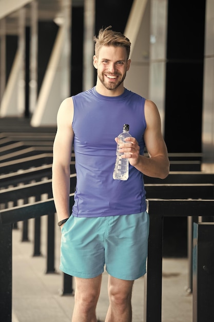 Concept de nutrition sportive Homme athlète tient une bouteille en plastique soin hydratation du corps après l'entraînement Boisson vitaminique rafraîchissante Athlète boit de l'eau après l' entraînement Homme apparence athlétique tient la bouteille d'eau