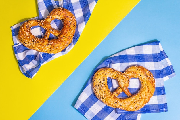 Photo concept d'oktoberfest - bretzels sur une serviette traditionnelle. lumière dure à la mode, ombre sombre. fond jaune-bleu pastel, vue de dessus