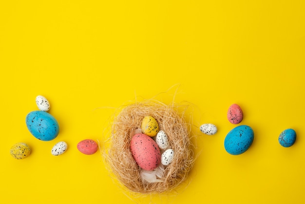 Concept de Pâques, des œufs multicolores dans un nid se trouvent sur une table jaune. - Copyspace