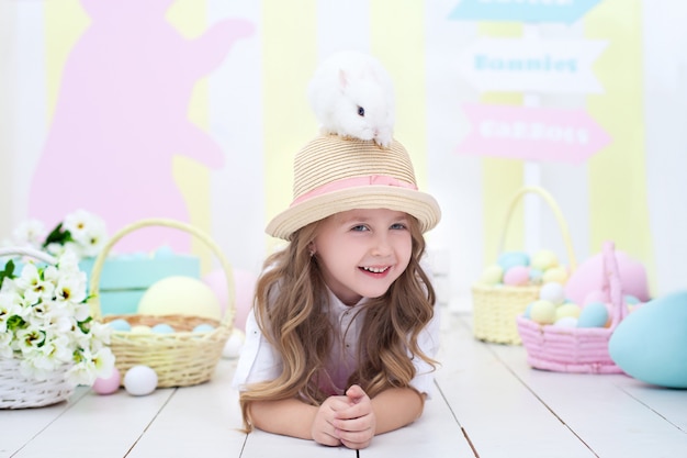 Concept de Pâques! Petite fille souriante tient un lapin de Pâques sur la tête. Décor de Pâques. Agriculture. Enfant et jardin. Petit fermier. Un enfant joue avec un lapin moelleux. Enfant et animal. Fleurs de printemps