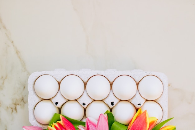 Photo concept de pâques, plat poser des œufs de poule et des tulipes colorées sur fond de marbre. vue de dessus.