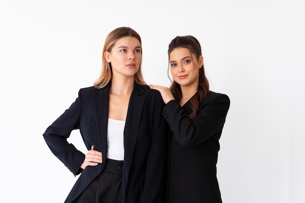 Concept de partenariat en affaires. Deux Jeune femme d'affaires vêtue d'un costume formel noir debout en studio isolé sur fond blanc. Une femme brune posa ses mains sur les épaules de son amie.