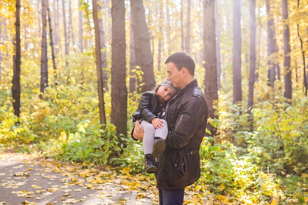 Concept de paternité, de famille et de loisirs - père tenant sa petite fille dans ses bras dans un parc d'automne