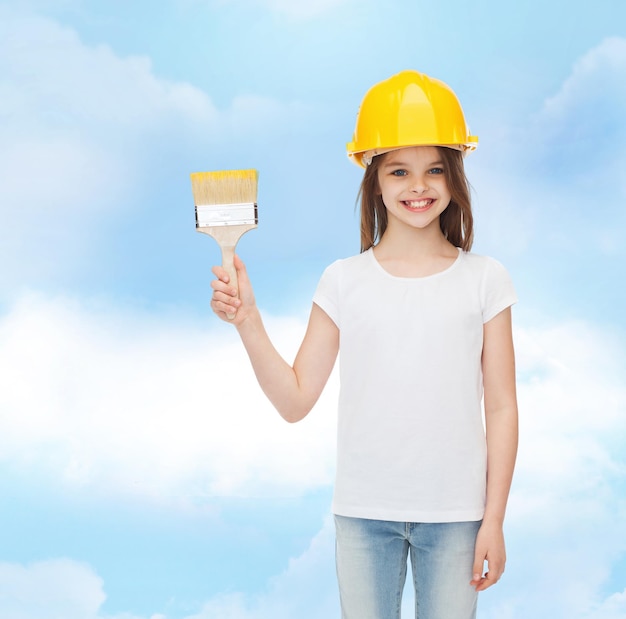 concept de peinture, de construction, d'enfance et de personnes - petite fille souriante dans un casque de protection avec un pinceau