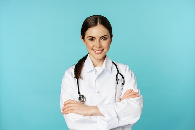 Concept de personnel médical et de médecins. Jeune femme médecin souriante, travailleur de la santé en blouse blanche et stéthoscope, à l'air confiant, patients en attente, fond bleu