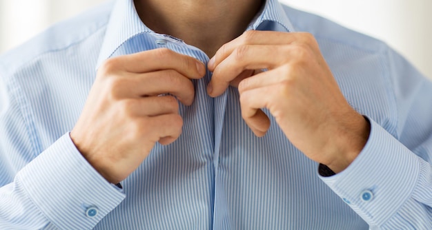concept de personnes, d'affaires, de mode et de vêtements - gros plan sur un homme qui s'habille et attache des boutons sur une chemise à la maison