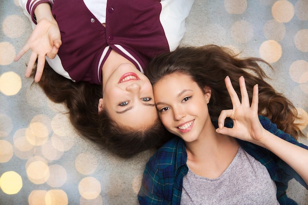 Photo concept de personnes, d'amis, d'adolescents et d'amitié - jolies adolescentes souriantes et heureuses allongées sur le sol sur fond de lumières de vacances